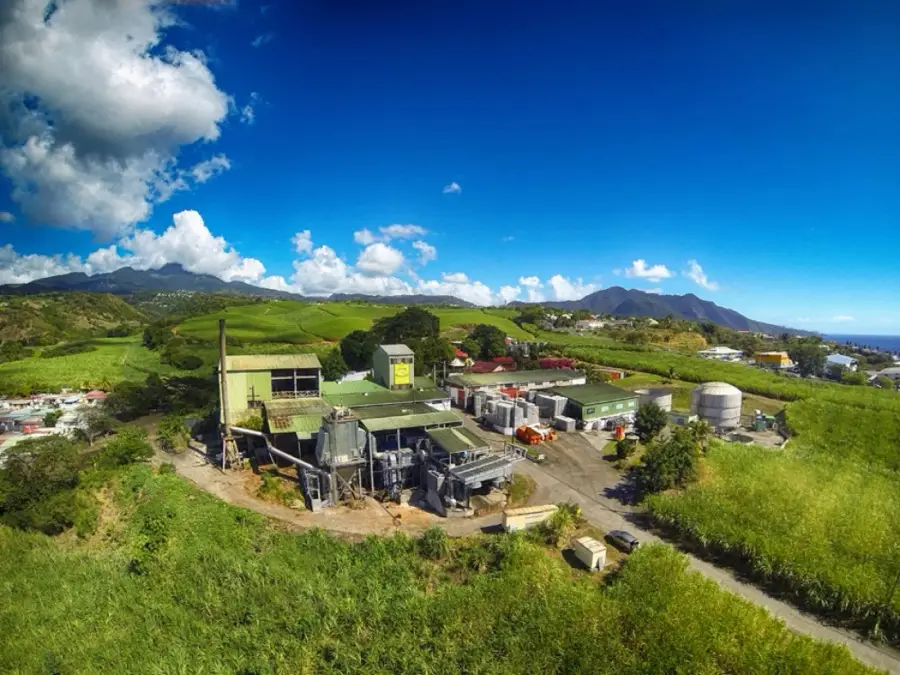 Vue aérienne de la Distillerie Bologne entourée de champs de canne, les mornes de Basse-Terre au fond