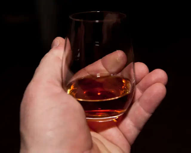 Verre de rhum vieux tenu au creux de la main pour la dégustation